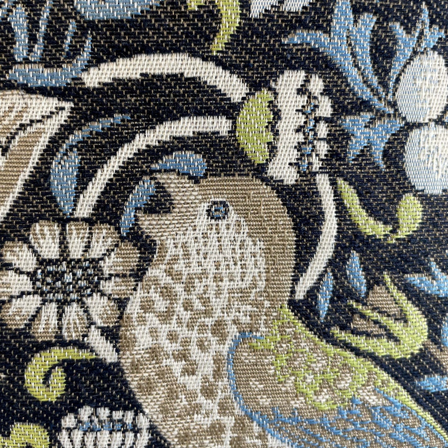 Macro of a woven bird figure — jacquard detail of William Morris's 1883 Strawberry Thief pattern.