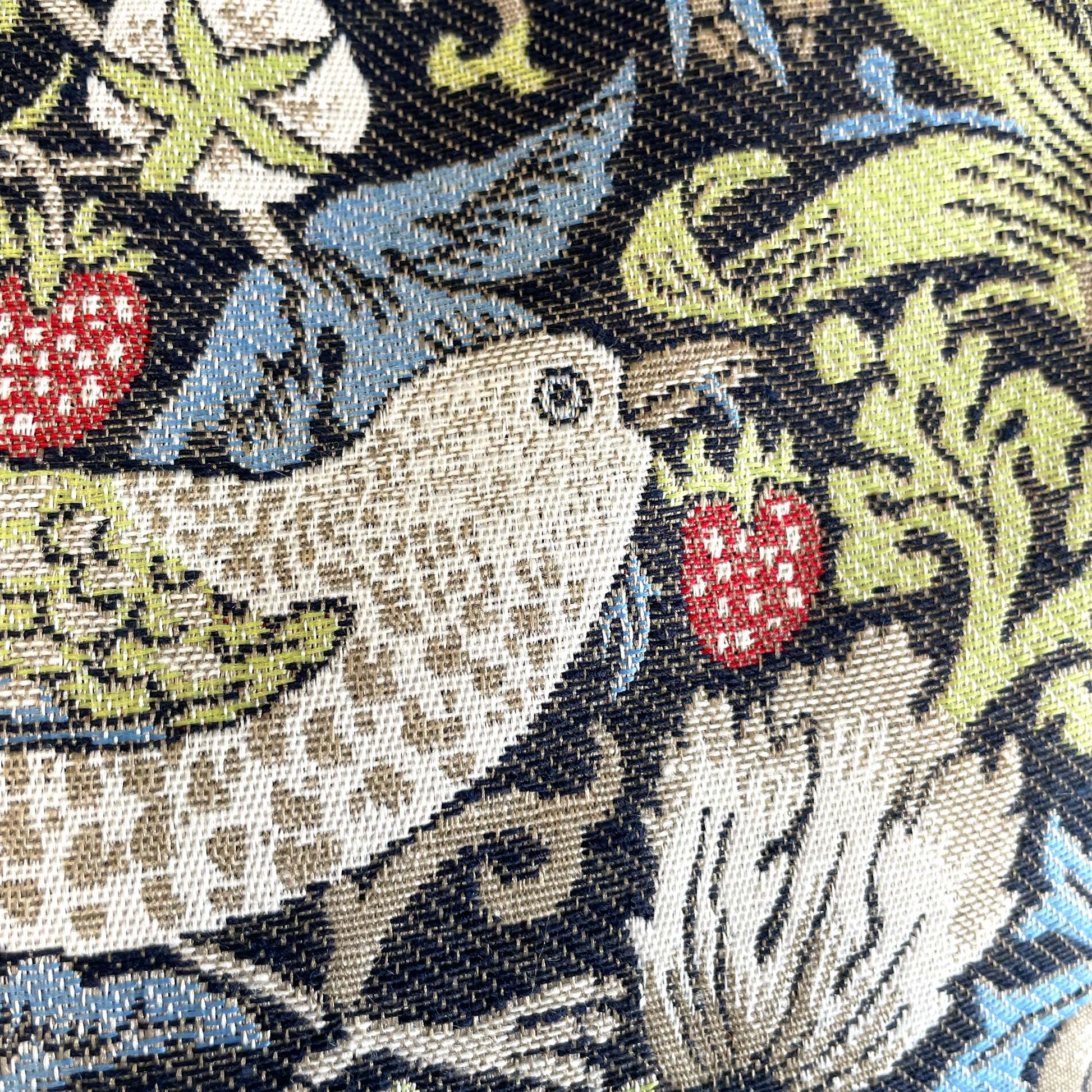 Close-up of a thrush holding a strawberry — woven jacquard detail of William Morris's 1883 Strawberry Thief pattern.
